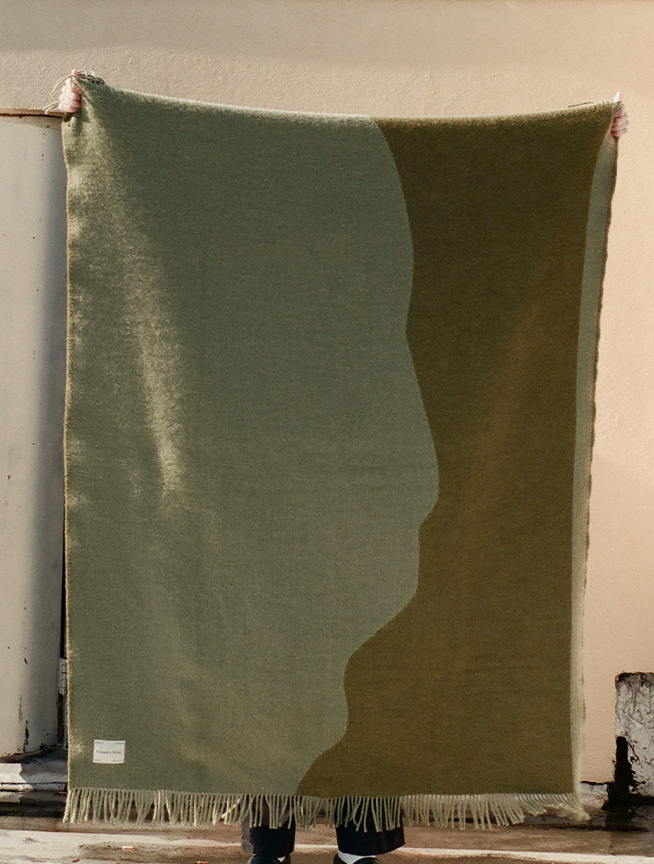 forestry-wool-stream-wool-blanket-moss-green-product-image-holding-up-blanket