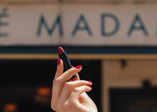 madame-gabriela-paris-at-7pm-red-lipstick-hand-with-red-nails-holding-lipstick-in-front-a-cafe-sign-saying-madame
