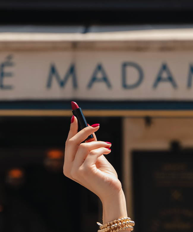 madame-gabriela-paris-at-7pm-red-lipstick-hand-with-red-nails-holding-lipstick-in-front-a-cafe-sign-saying-madame