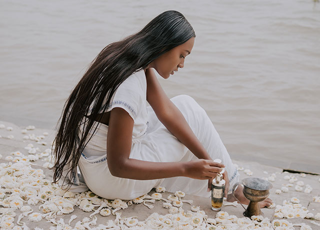 Model exploring the meaning of Ayurveda by practicing an Ayurvedic skincare ritual besides a river