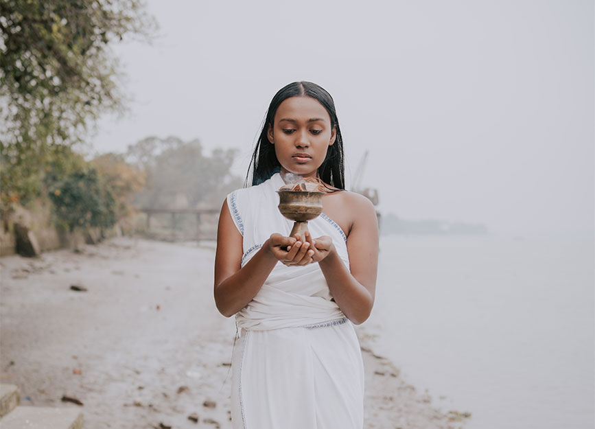 Model exploring the meaning of Ayurveda by practicing an Ayurvedic skincare ritual besides a river