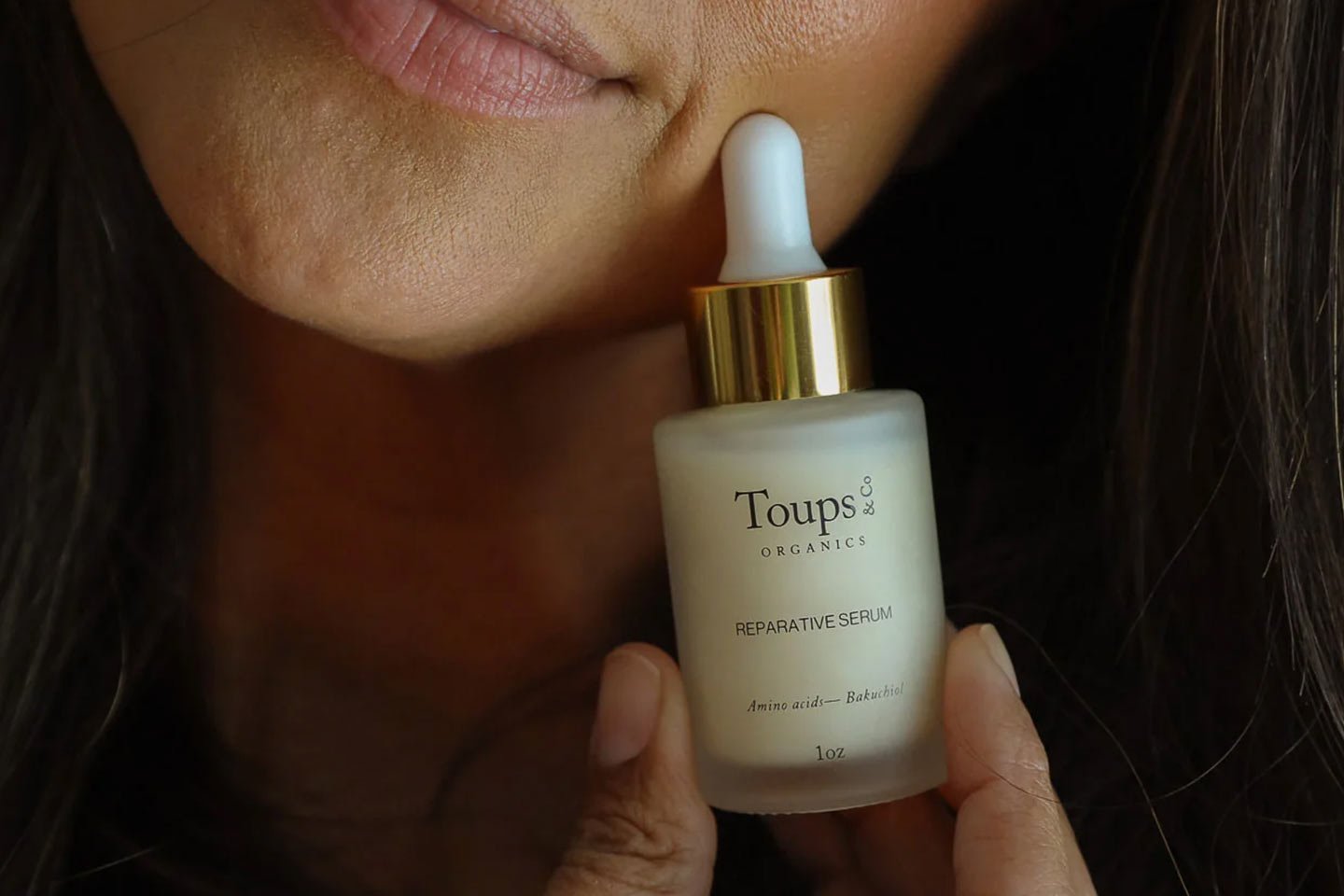 A woman holding a Toups & Co bottle of serum up to her face
