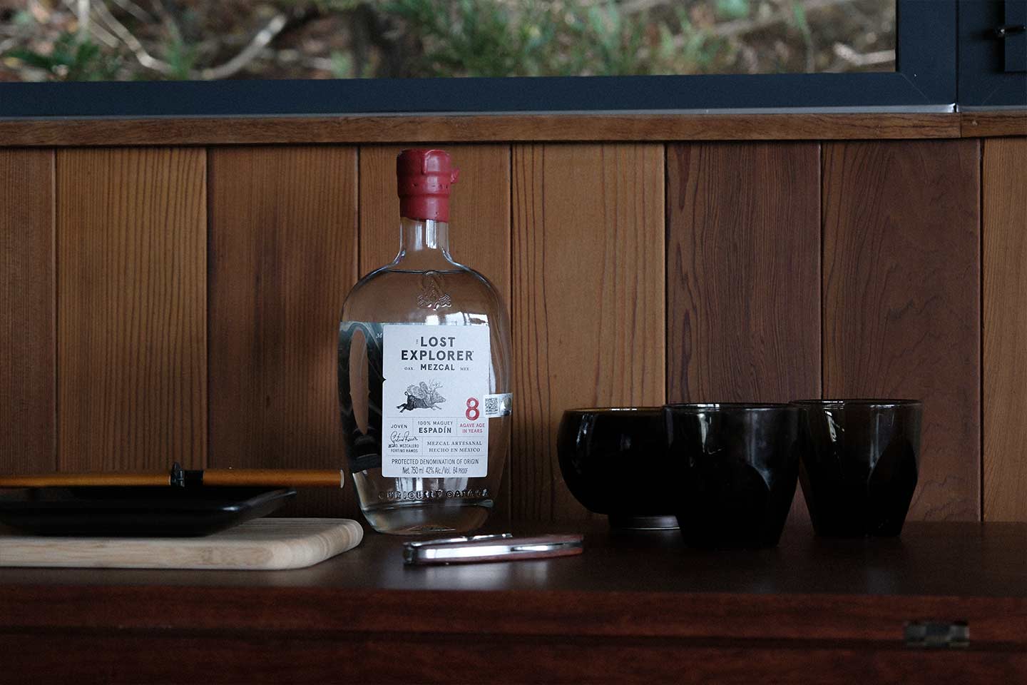 A bottle of Lost Explorer Mezcal sitting on a table with a wooden wall background