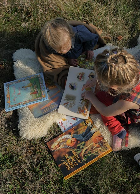 Two young girls reading books outside on a sheepskin rug
