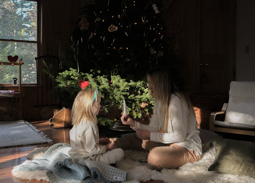 A mother teaching her daughter how to play with cards in front of a Christmas tree