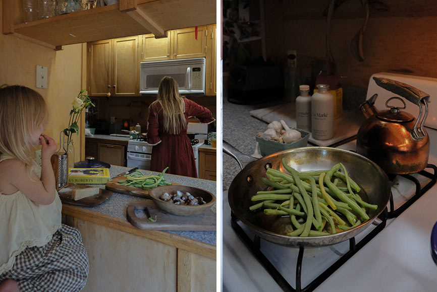 A young child eating fresh green beans while her mother cooks in the kitchen