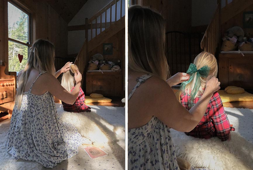 A mother brushing her daughter's hair and putting in a green bow