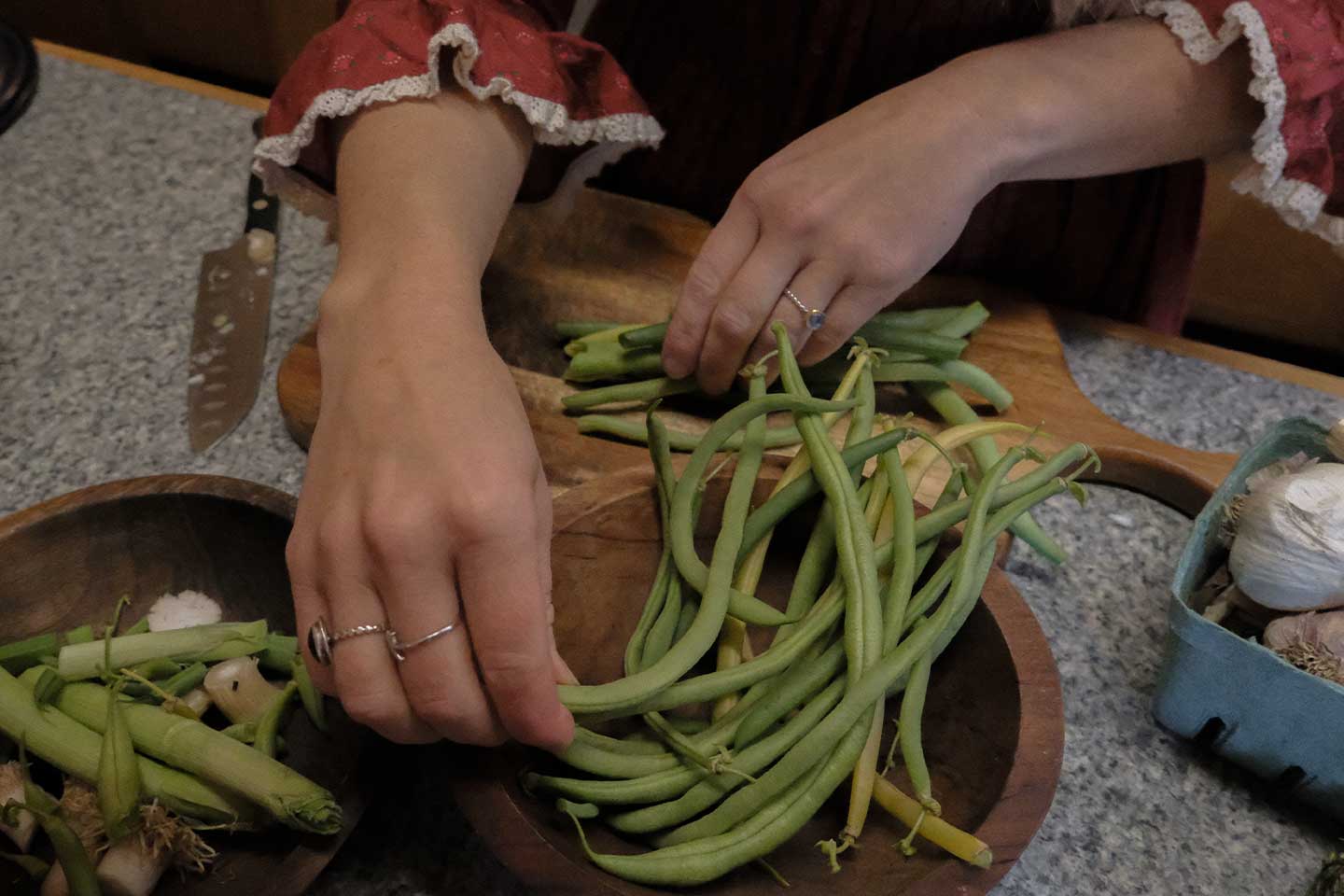 A woman cleaning fresh green beans in a wooden bowl