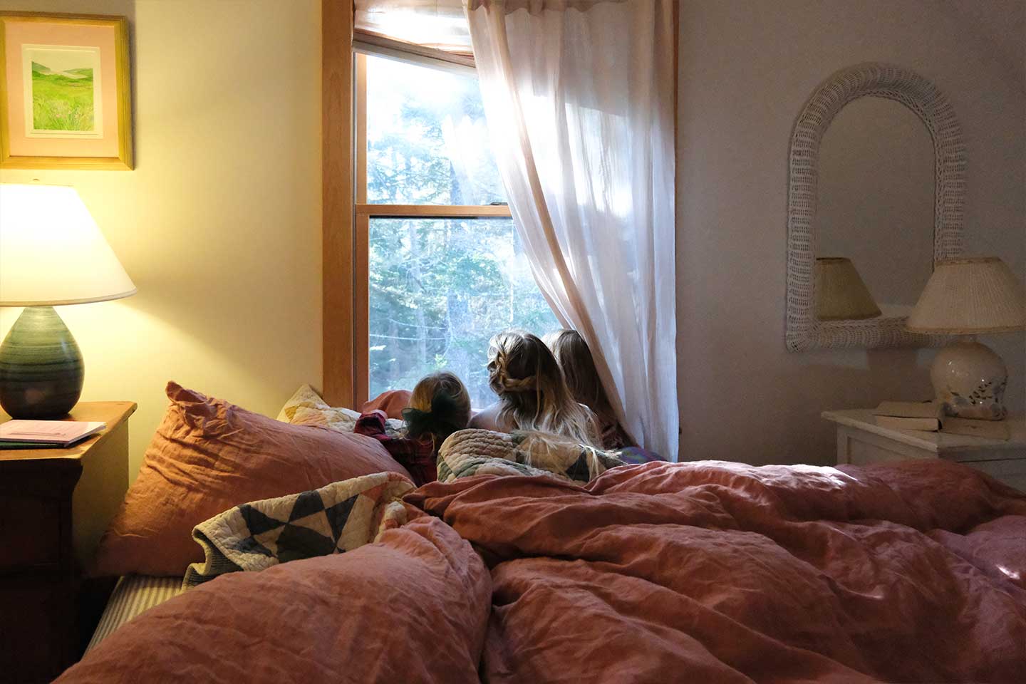 A family in bed with pink sheets looking out of the window