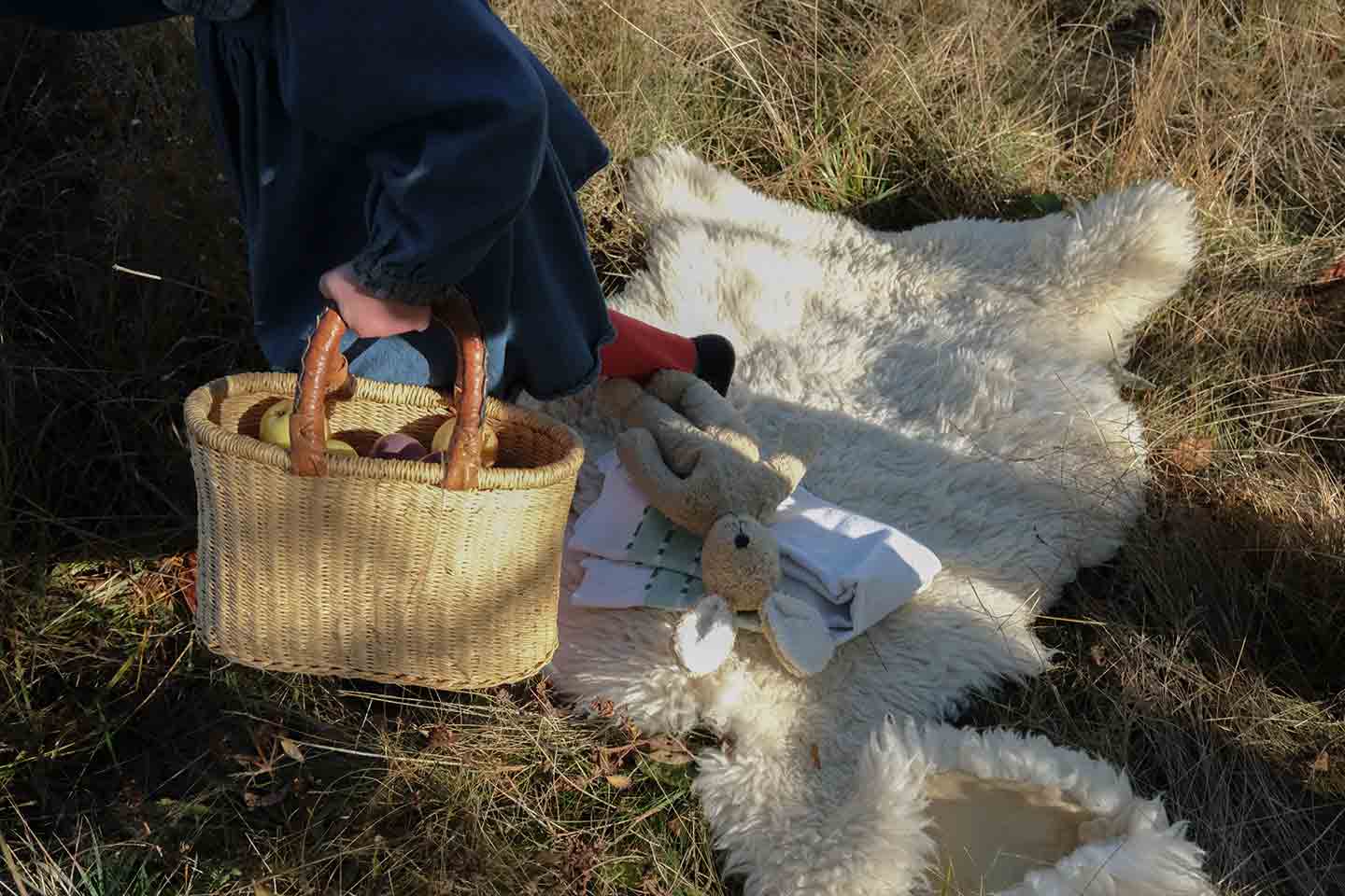 A child walking off of a sheepskin rug with a basket of apples in her hand