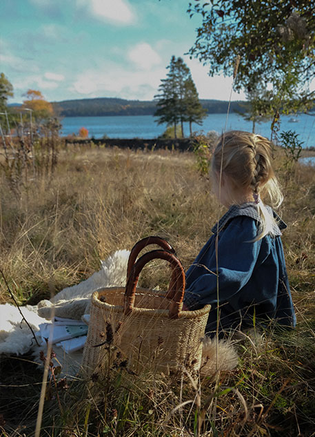 A little girl sitting in a meadow with a wicker basket next to her