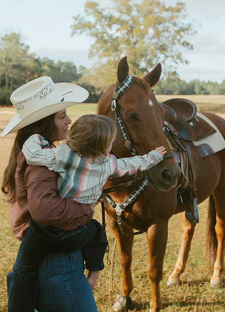 A woman holding her child petting a horse
