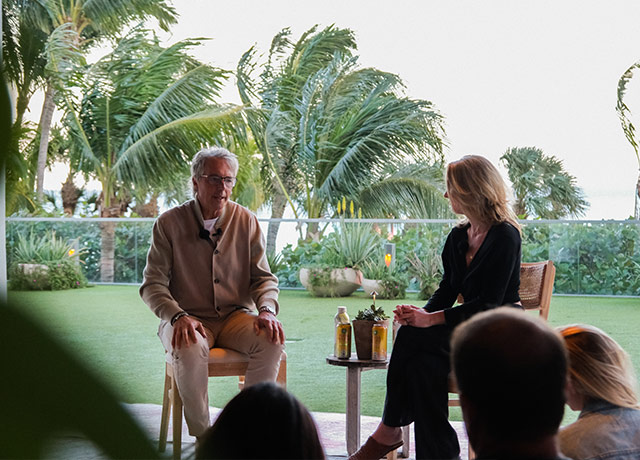 Dan Buettner of Blue Zones speaks to Cora Hilts with a backdrop of palm trees