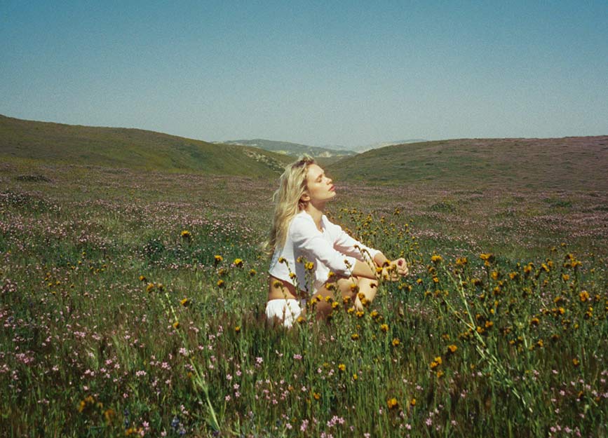 A woman sitting in a meadow in white cotton lingerie