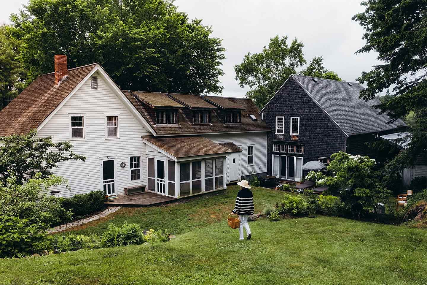 A woman carrying a basket of flowers into an old farmhouse in Maine