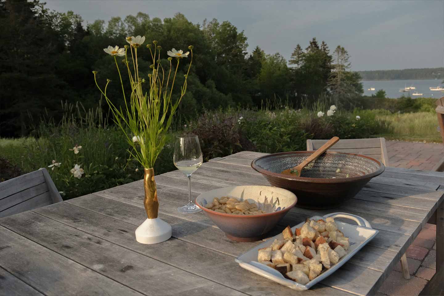 An outdoor dining table on a patio with a panzanella salad and flowers