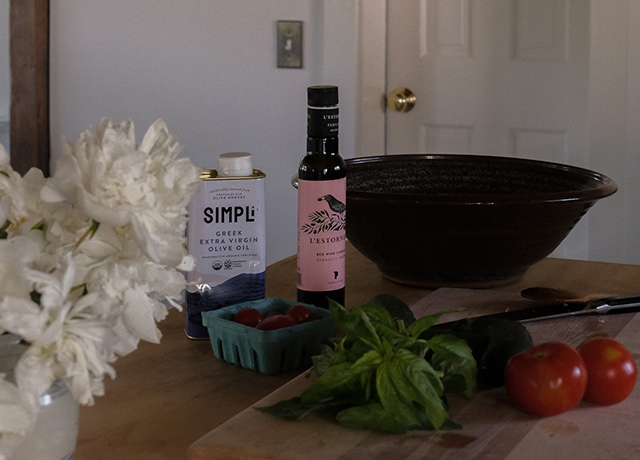 A kitchen with olive oil, vinegar, a large bowl and a vase of peonies